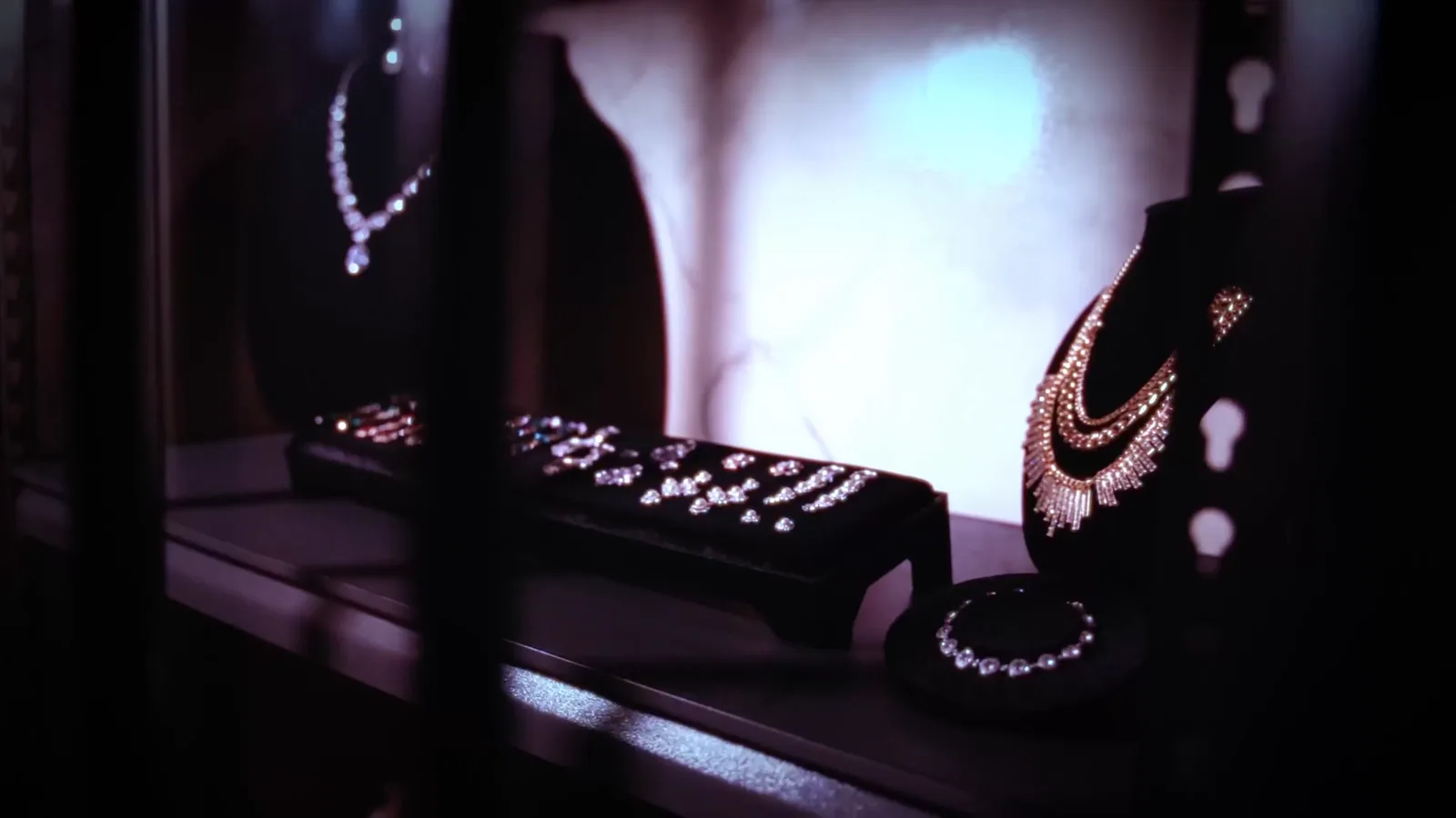 Necklaces and jewellery on display stands behind bars in Bank Heist